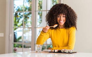 Poster - African american woman eating sushi using chopsticks at home with a happy face standing and smiling with a confident smile showing teeth