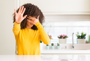 Canvas Print - African american woman wearing yellow sweater at kitchen covering eyes with hands and doing stop gesture with sad and fear expression. Embarrassed and negative concept.