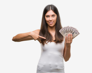 Poster - Young hispanic woman holding dollars with surprise face pointing finger to himself