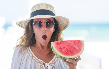 Wall Mural - Middle age brunette woman by the sea eating watermelon scared in shock with a surprise face, afraid and excited with fear expression