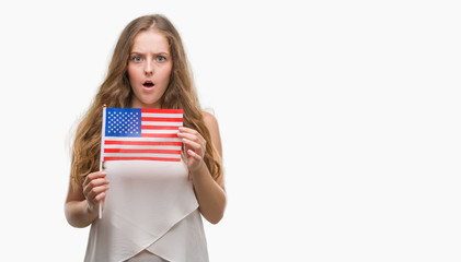 Sticker - Young blonde woman holding flag of USA scared in shock with a surprise face, afraid and excited with fear expression