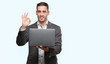 © Krakenimages.com - Handsome young man using computer laptop doing ok sign with fingers, excellent symbol