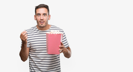 Sticker - Handsome young man eating popcorn scared in shock with a surprise face, afraid and excited with fear expression