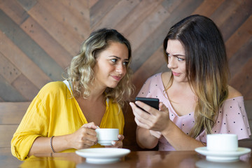 Cringed female friends reading message on smartphone. Two pretty women discussing strange text message in cafe. Technology and life concept 