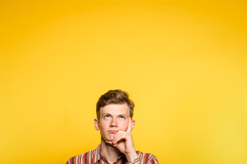 Wall Mural - pensive thoughtful not impressed man looking up. portrait of a young guy on yellow background popping up or peeking out from the bottom. free space for advertisement.