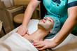 © fotofrol - Beautiful young woman lying on massage table while facial mask is put on her face.