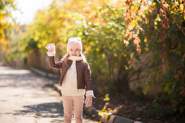 Autumn children's fashion. A little girl dances, jumps and rejoices in the fall against a background of yellow and red foliage on trees and bushes. Joy and happiness