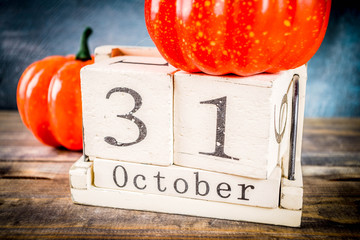 Halloween celebration concept with pumpkin decoration, candy, jack o lantern cup and old retro styled wooden calendar, blue and wooden background, copy space