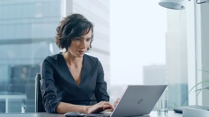 Sticker - Confident Businesswoman Sitting at Her Desk and Working on a Laptop in Her Modern Office. Stylish Beautiful Woman Doing Important Job. In the Window Big City Business District View. 