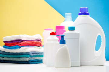 Wall Mural - Photo of several bottles of cleaning products and colored towels on table isolated on blue, yellow background