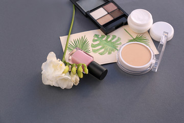 Set of decorative cosmetics with flowers on gray background