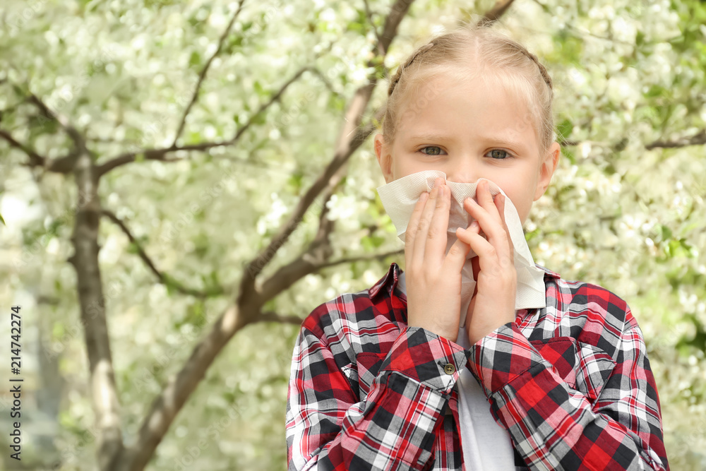 Little girl with nose wiper near blooming tree. Allergy concept
