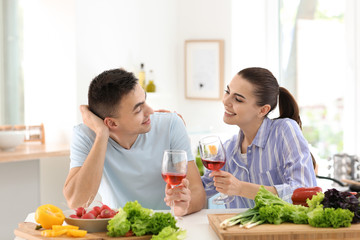 Wall Mural - Young couple drinking wine while cooking together in kitchen