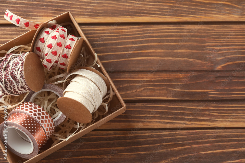 Box with ribbons and tapes for scrapbooking on wooden background