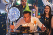 Young man blowing out candles on birthday cake at party in club
