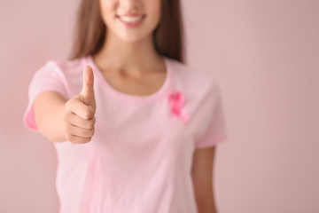 Canvas Print - Beautiful woman with pink ribbon showing thumb-up gesture on color background. Breast cancer concept