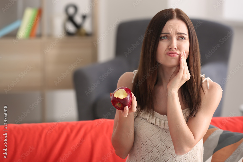 Young woman with sensitive teeth and apple on sofa at home