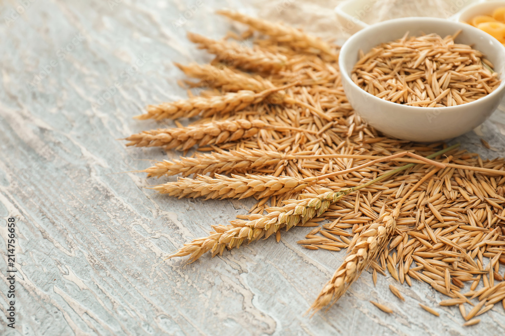 Bowl with oat grains and wheat spikelets on wooden background
