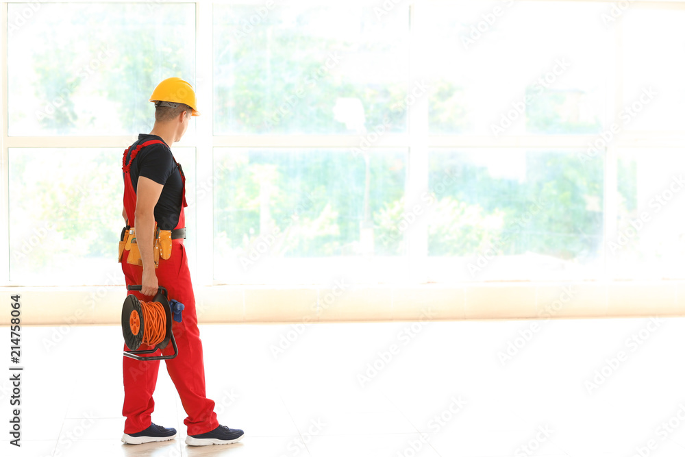 Electrician with extension cord reel in new empty apartment