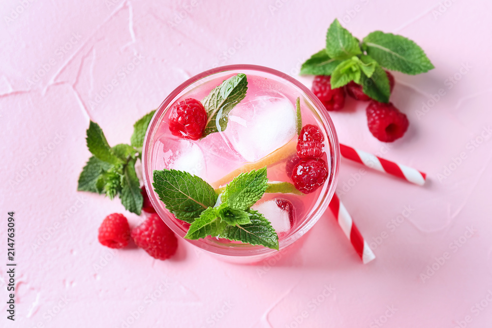 Glass of fresh raspberry mojito on color background