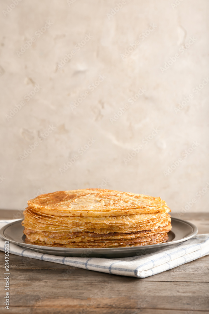 Plate with stack of tasty thin pancakes on wooden table