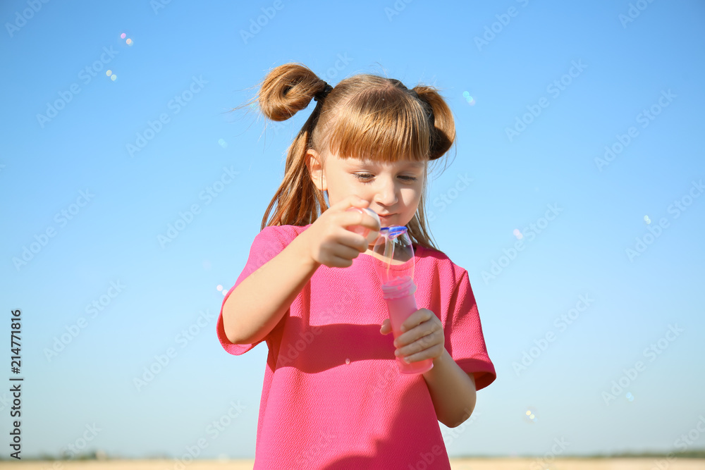 Cute little girl blowing soap bubbles on sunny day