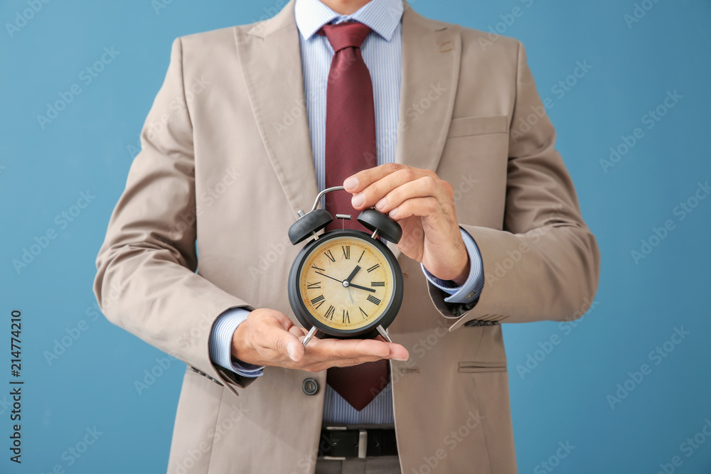 Businessman holding alarm clock on color background. Time management concept