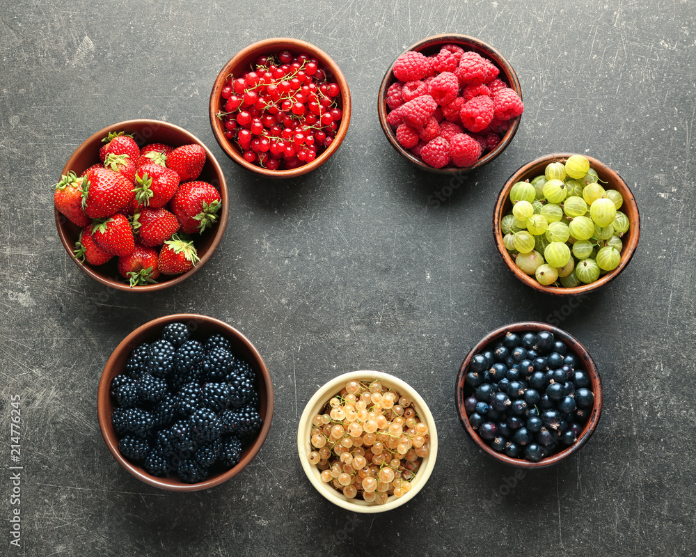 Bowls with various ripe berries on grey background, top view