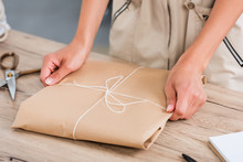 Cropped Image Of Female Fashion Designer Wrapping Paper Package At Table
