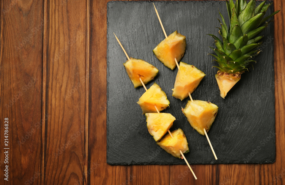 Sticks with pieces of ripe pineapple on slate plate