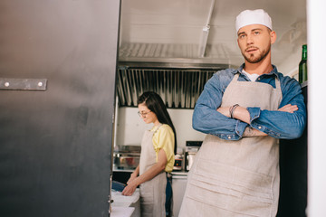 Poster - male chef standing with crossed arms while female colleague working behind in food truck