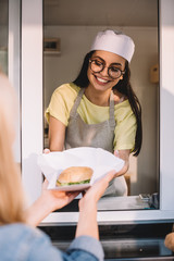 Wall Mural - Cropped image of smiling chef giving burger to customer in food truck