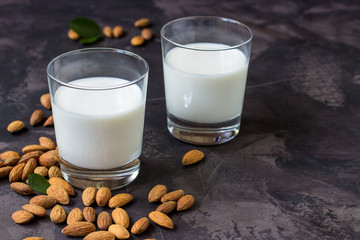 Almond milk in glass and almonds nuts on a dark background