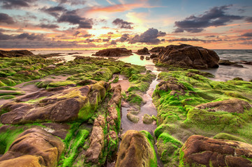 view of beautiful sunset sky at unknown beach in Sabah, Malaysia. Natural coastal rocks covered by green moss on the ground. soft focus due to long expose.