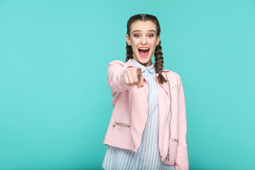 Wall Mural - wow, amazed portrait of beautiful cute girl standing with makeup and brown pigtail hairstyle in striped light blue shirt pink jacket. indoor, studio shot isolated on blue or green background.