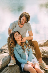 Stylish young couple. Film photo with a light and a sunlight. The guy with a stylish haircut, and with hair on the shoulders stroking red-haired girl. Background stones and river