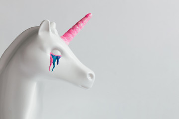 Wall Mural - White painted unicorn head with colorful tears and pink horn on bright white background. Minimal art fantasy concept.