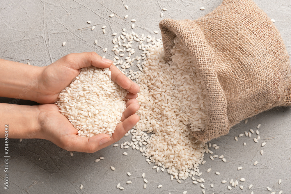 Female hands with heap of raw rice on textured background