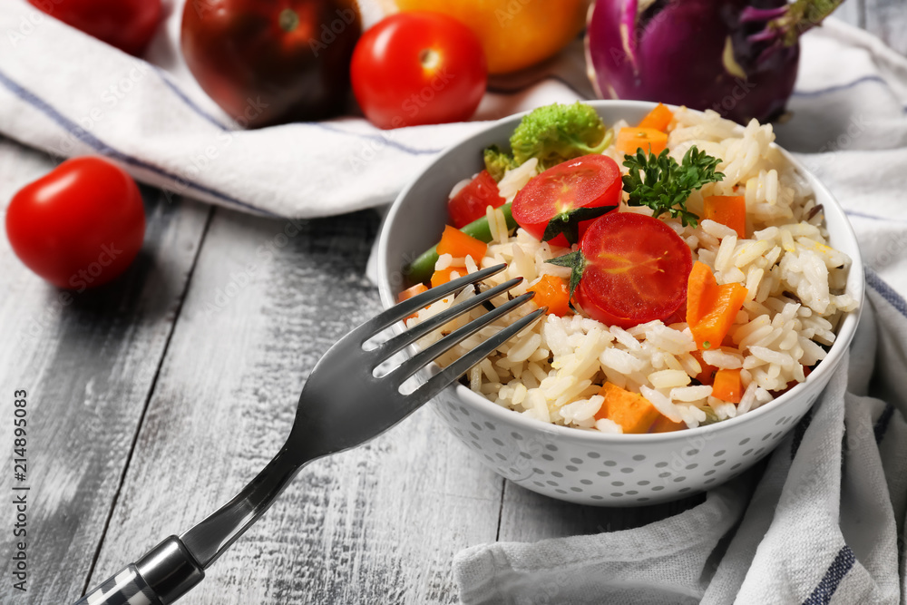 Bowl with tasty boiled rice and vegetables on wooden table