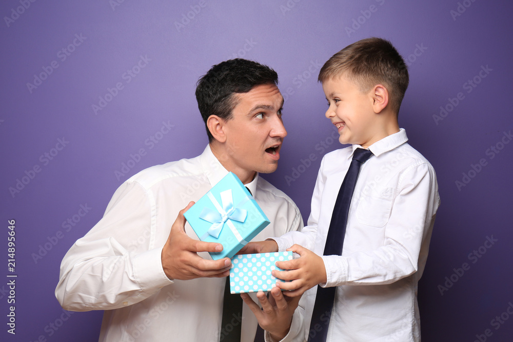 Little boy giving present to his father on color background