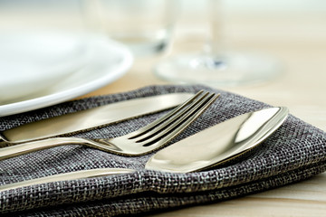 A set of bronze cutlery, spoon, fork and knife arrange on napkin with white dish on wooden table