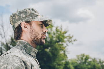 Wall Mural - side view of confident soldier in military uniform with cloudy sky on background