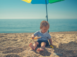 Little toddler sitting under parasol on beach