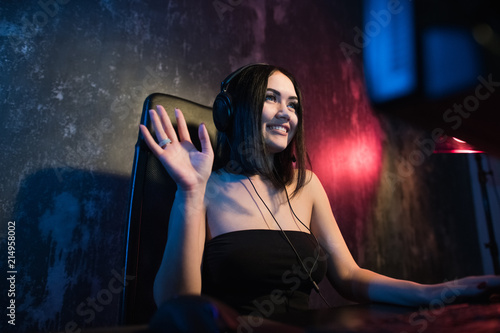 Fotografie, Obraz A cute female gamer girl sits in a cozy room behind a computer and plays games