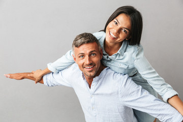 Wall Mural - Portrait of joyful caucasian people man and woman in basic clothing smiling and hugging together, isolated over gray background