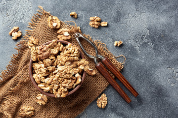 Wall Mural - Walnut kernels in clay bowl. Nuts and nutcracker on gray background. Top view.