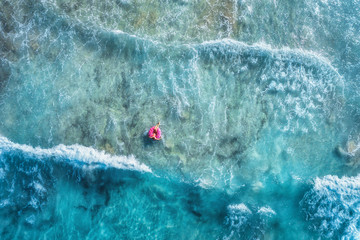 Wall Mural - Aerial view of slim young woman swimming on the donut swim ring in the transparent blue sea with waves at sunset. Tropical aerial landscape with girl, clear water in Spain. Top view. Summer travel