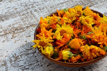 Flowers of  calendula in a ceramic plate on a wooden table in the style of rustic close-up.