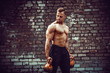 © zamuruev - Athletic man working out with a kettlebell in front of brick wall. Strength and motivation. Outdoor workout. Biceps exercise.