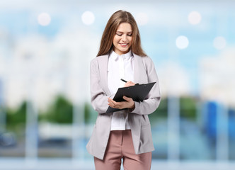 Wall Mural - Young businesswoman in elegant suit with clipboard on blurred background